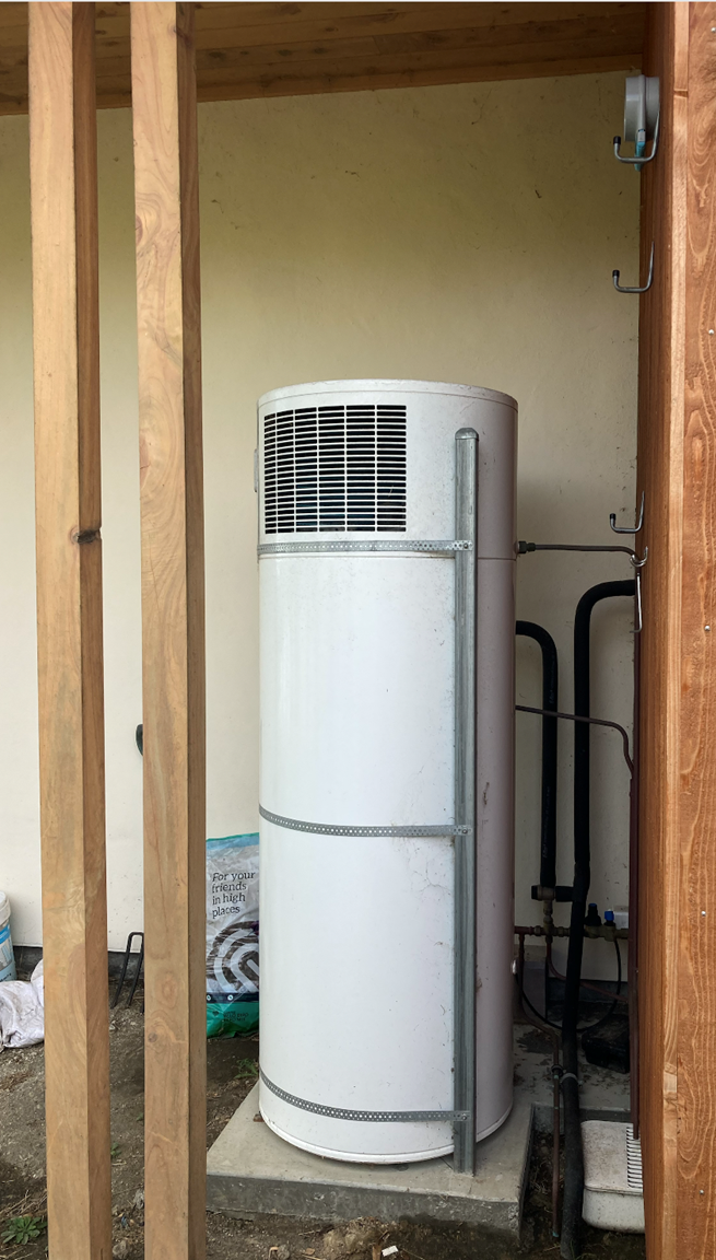 A heat pump hot water heater installed outside in New Zealand, appropriately sheltered